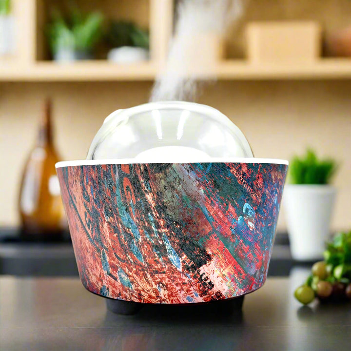 Artistic Essence Oil Diffuser, a masterful creation from Emilio Horton, founder of YOU ME &amp; EMILIO. Featuring a vibrant, textured abstract design of deep blues, fiery reds, and shimmering gold, this diffuser transforms any space into a sanctuary of creativity, relaxation, and sensory delight.

More than just an aromatherapy tool, the Artistic Essence brings an immersive experience with the gentle sound of running water and soft mist creation, inspired by the tranquility of natural streams.