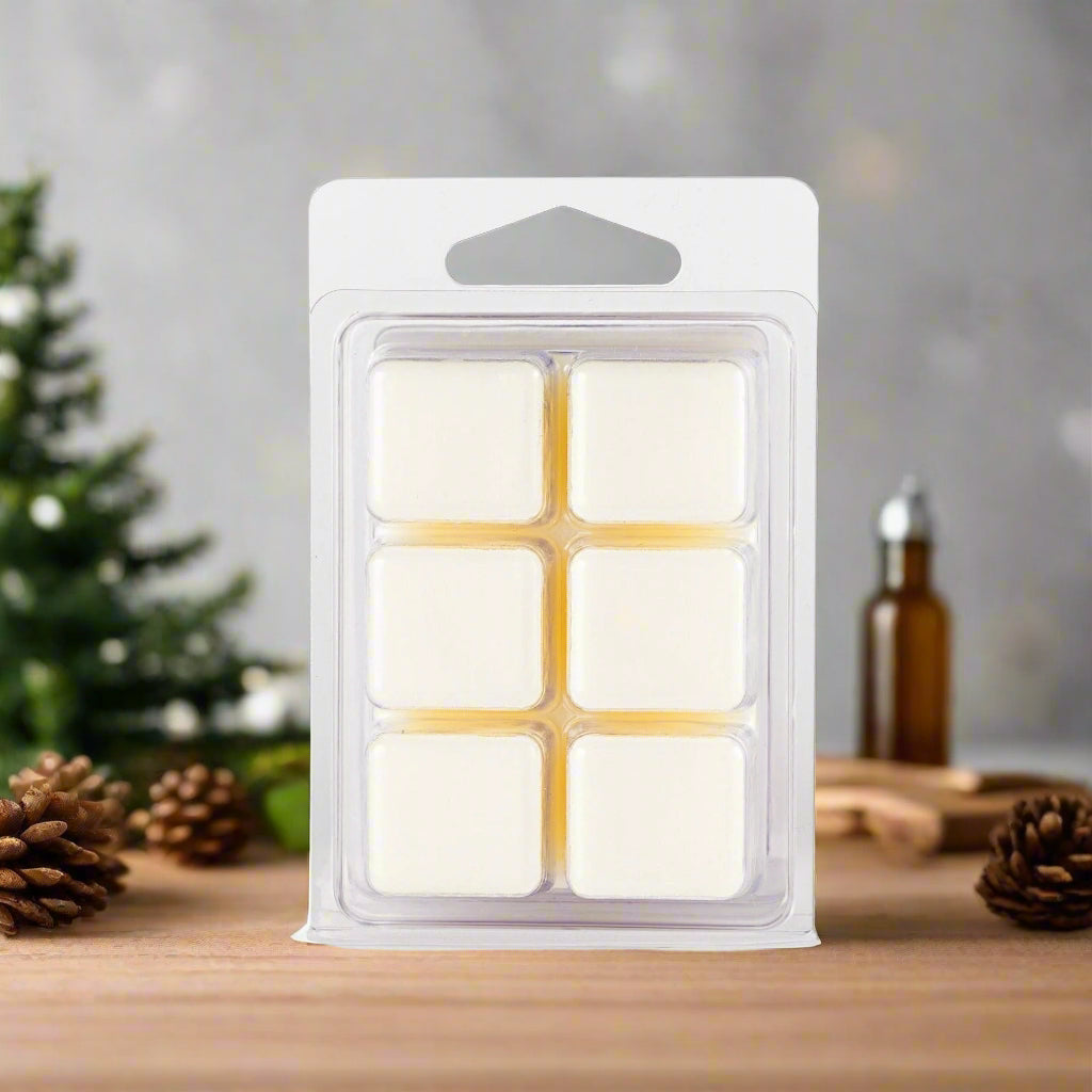 Christmas Wreath Soy Wax Melts in a clear clamshell, placed on a wooden table with seasonal greenery, cinnamon sticks, and a glowing candle in the background.