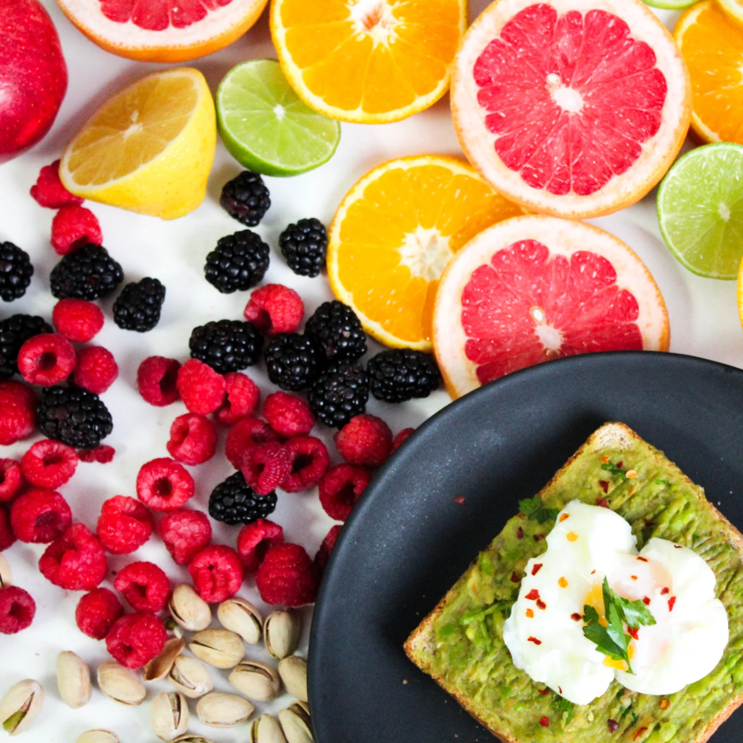 Assorted fruits, including citrus and berries, with a plate of avocado toast topped with sour cream and greens.
