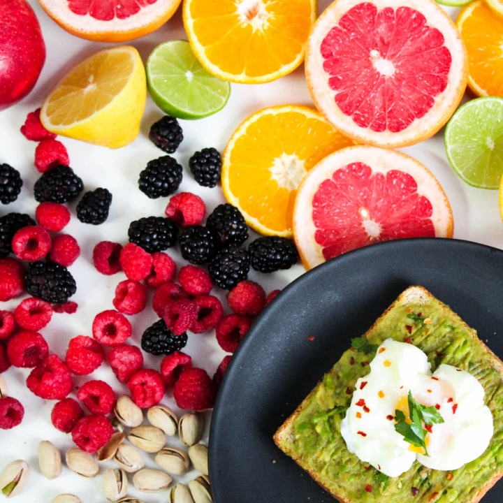 Assorted fruits, including citrus and berries, with a plate of avocado toast topped with sour cream and greens.