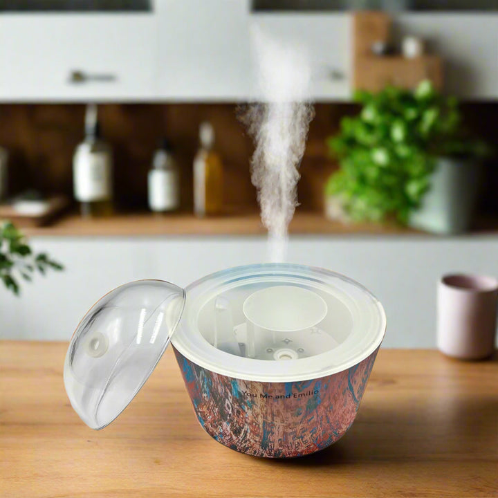 Artistic Essence Oil Diffuser, a masterful creation from Emilio Horton, founder of YOU ME & EMILIO. Featuring a vibrant, textured abstract design of deep blues, fiery reds, and shimmering gold, this diffuser transforms any space into a sanctuary of creativity, relaxation, and sensory delight.

More than just an aromatherapy tool, the Artistic Essence brings an immersive experience with the gentle sound of running water and soft mist creation, inspired by the tranquility of natural streams.