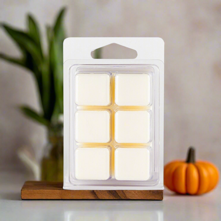 Pack of wax melts on a wooden block with a pumpkin and plant in the background