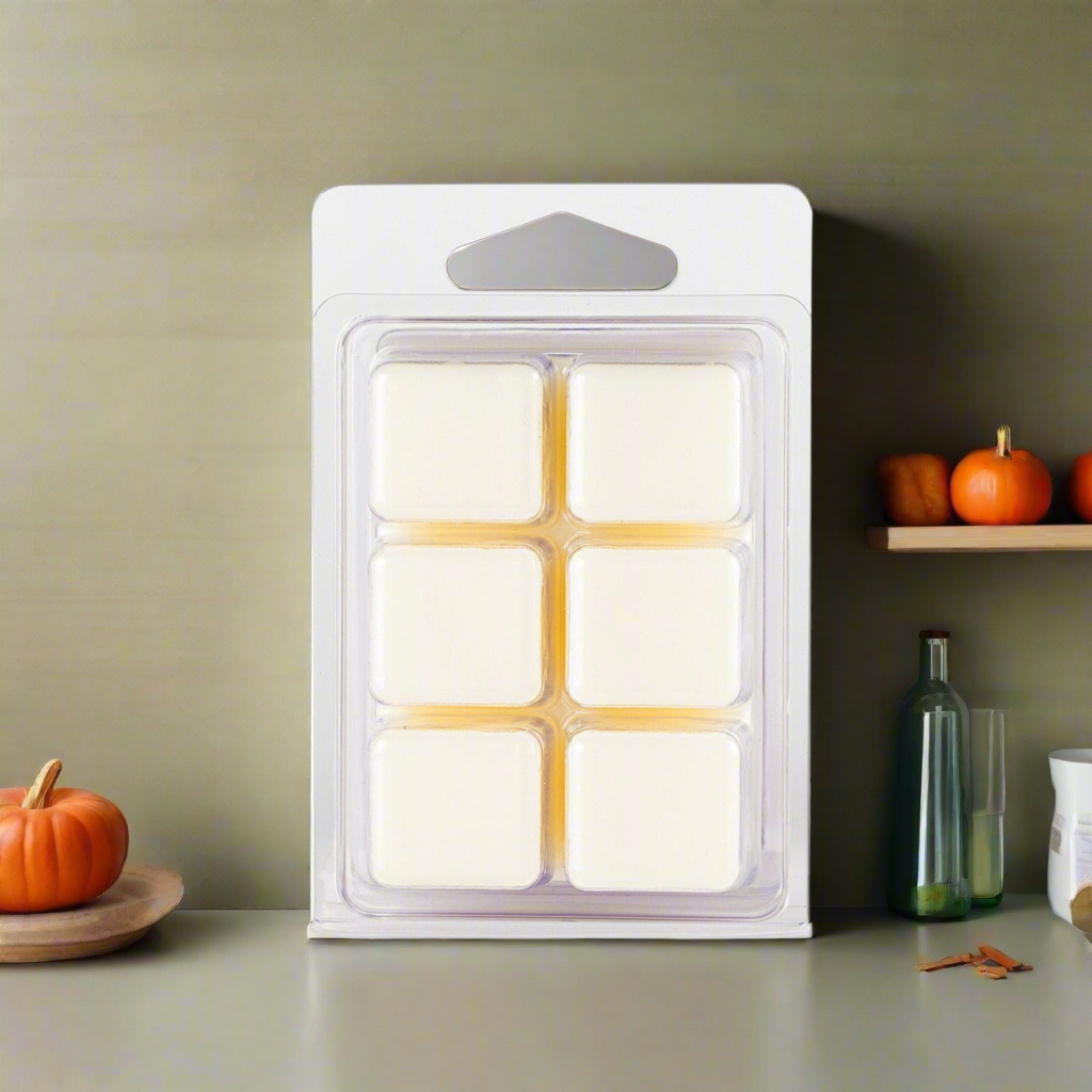 Pack of six white wax melts in a clear plastic packaging on a neutral background with pumpkins.