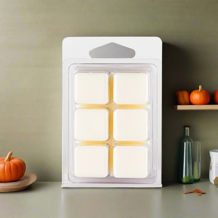 Pack of six white wax melts in a clear plastic packaging on a neutral background with pumpkins.