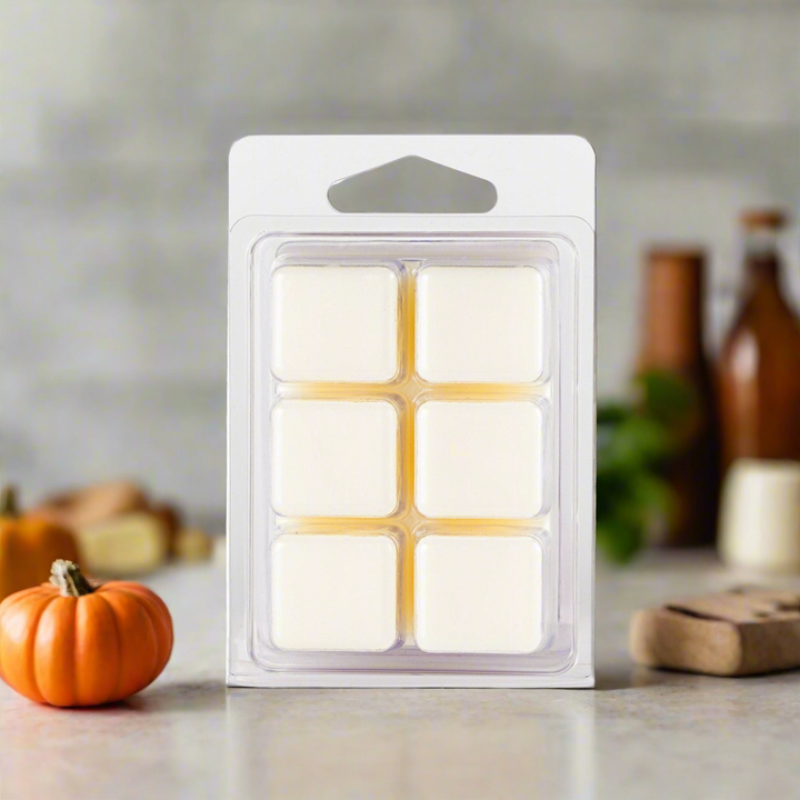 Pack of six wax melts in a clear plastic packaging on a neutral background with decorative items.