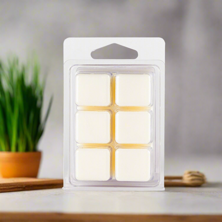 Pack of six white wax melts in a clear plastic packaging on a neutral background with a plant and wooden surface.