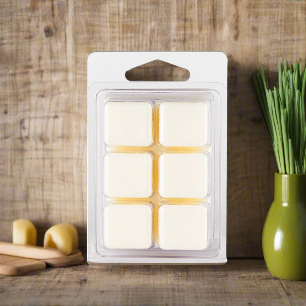 Pack of wax melts in a clear windowed packaging on a wooden surface with a vase and bread in the background.