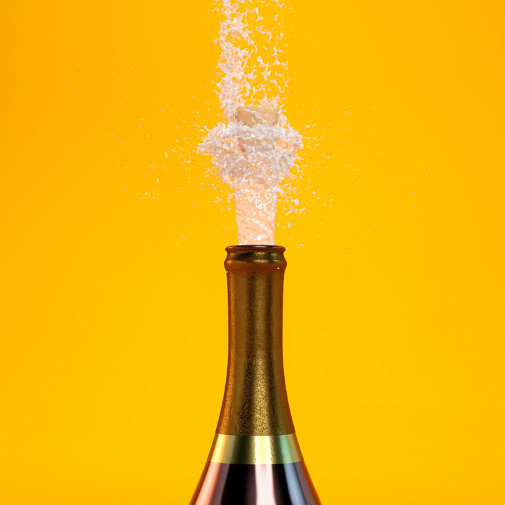 Bottle of champagne with cork popping against a yellow background