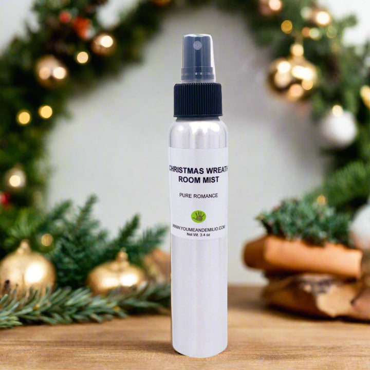 Polished cylindrical aluminum bottle of Christmas Wreath Room Mist displayed on a festive tray, with snow-dusted pine needles, cinnamon sticks, and warm lights.